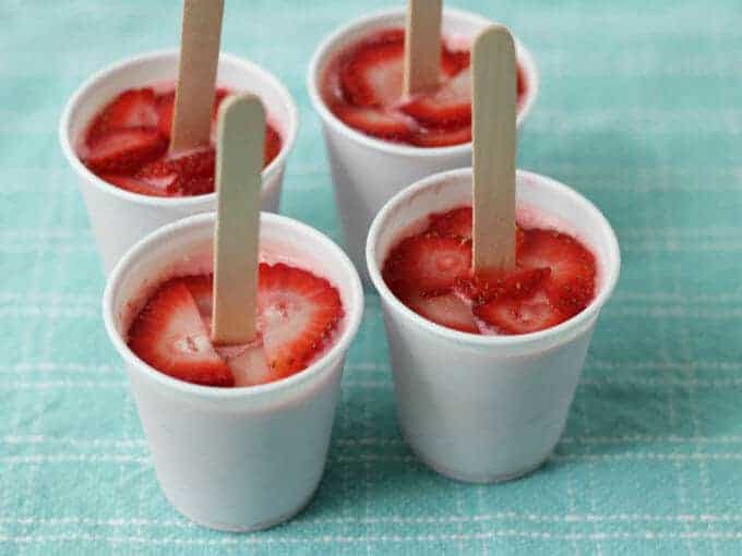 strawberry popsicles in plastic cups with popsicle sticks