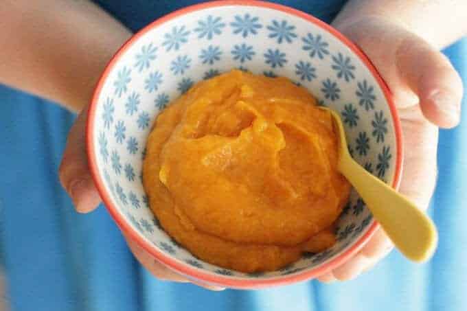 healthy mashed sweet potatoes in blue floral bowl with child's hands