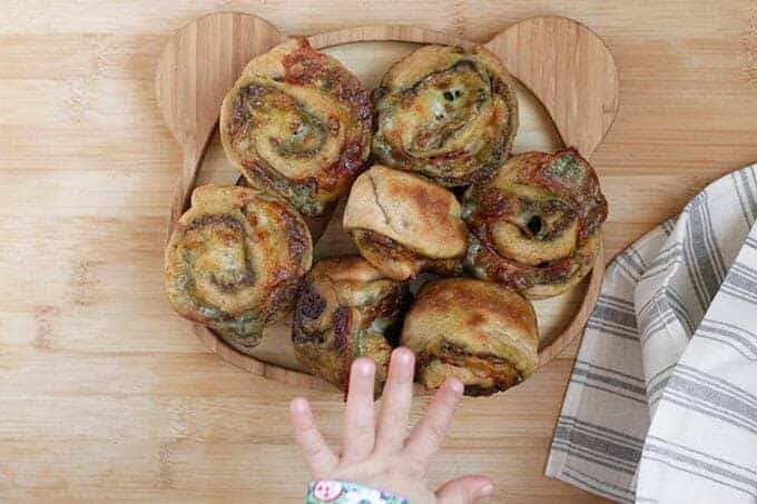 homemade pizza rolls with pesto on cuttin g board with toddler hand
