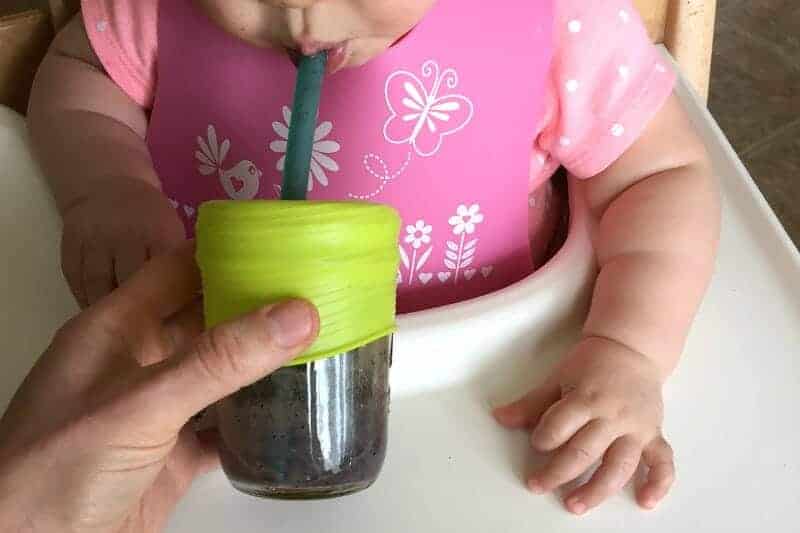 baby drinking cup of blueberry banana smoothie with silicone top and straw