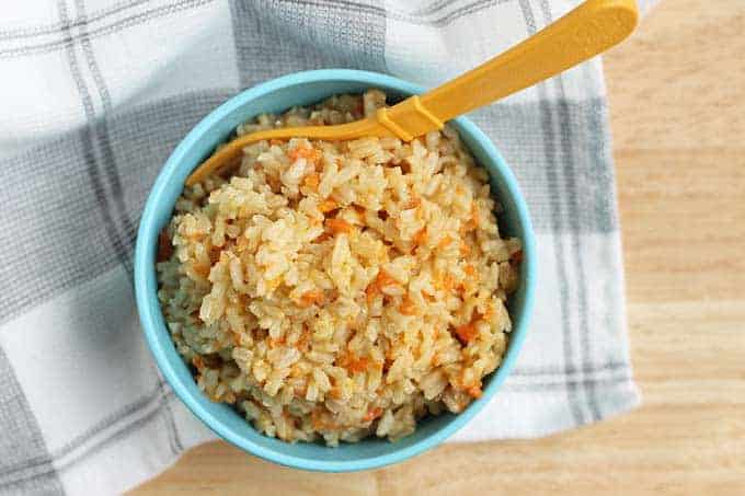 cheesy rice with carrots in blue bowl with yellow spoon