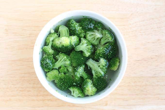 thawing frozen broccoli in water in white bowl