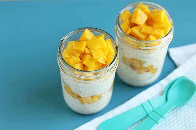 mango overnight oats with yogurt layered in mason jars with teal spoon
