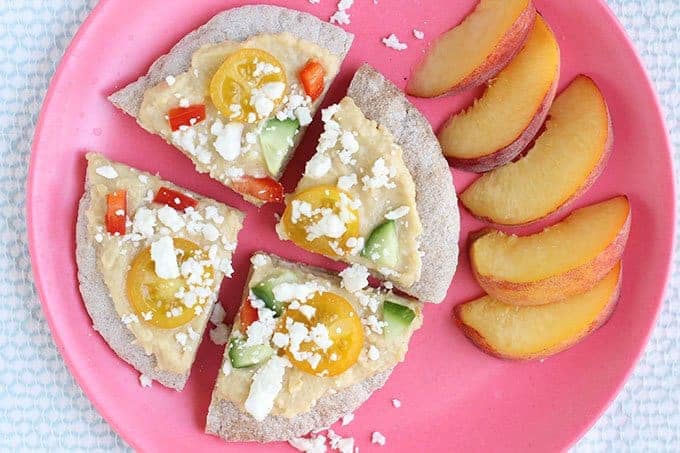 sliced pita pizza with hummus and veggies on pink plate