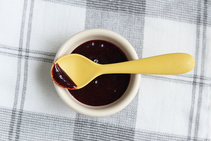 blueberry puree in white bowl with yellow baby spoon