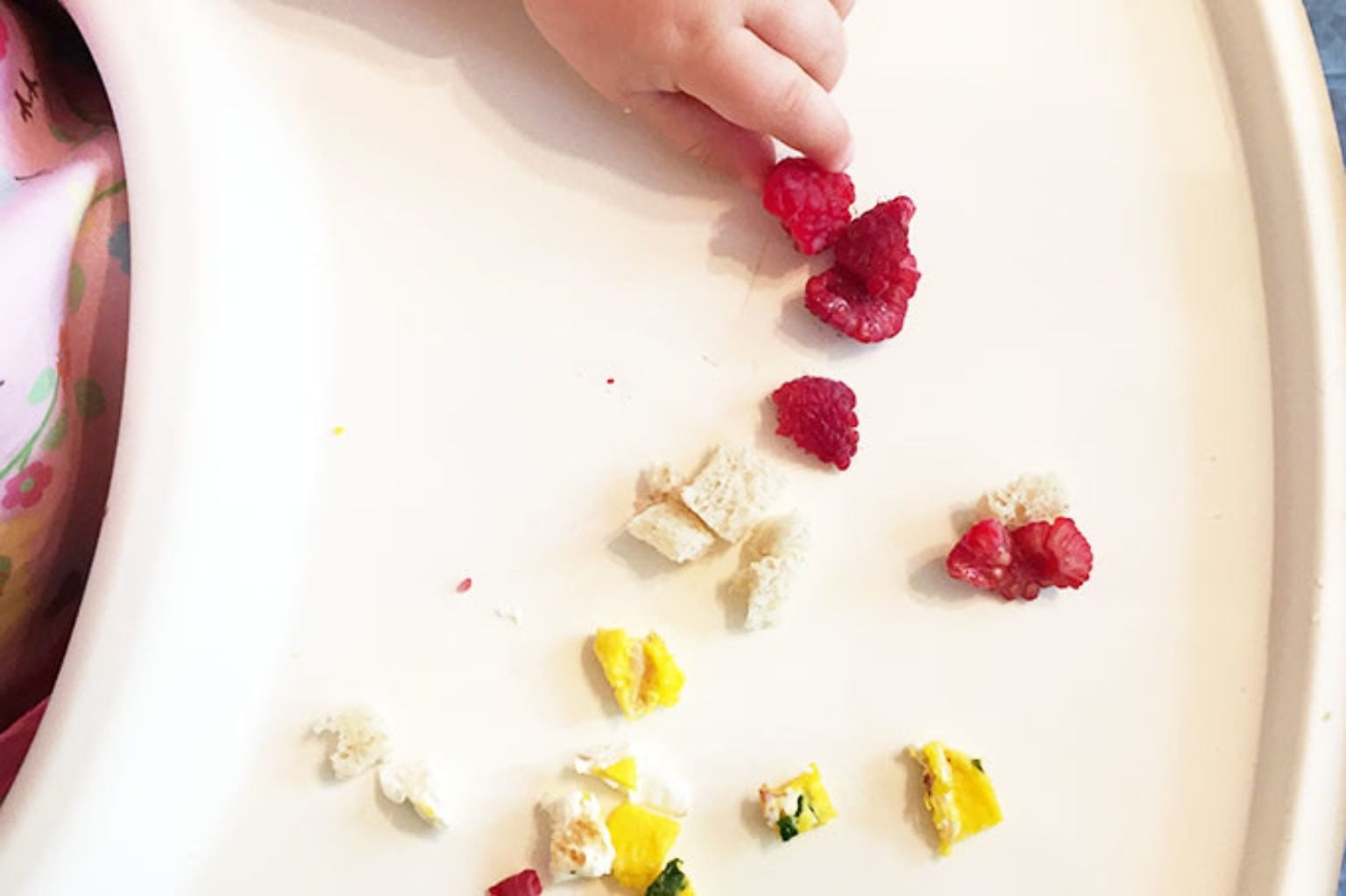 baby hand with raspberries and egg on highchair.