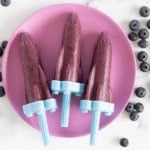 Blueberry popsicles on purple plate with blueberries on side.