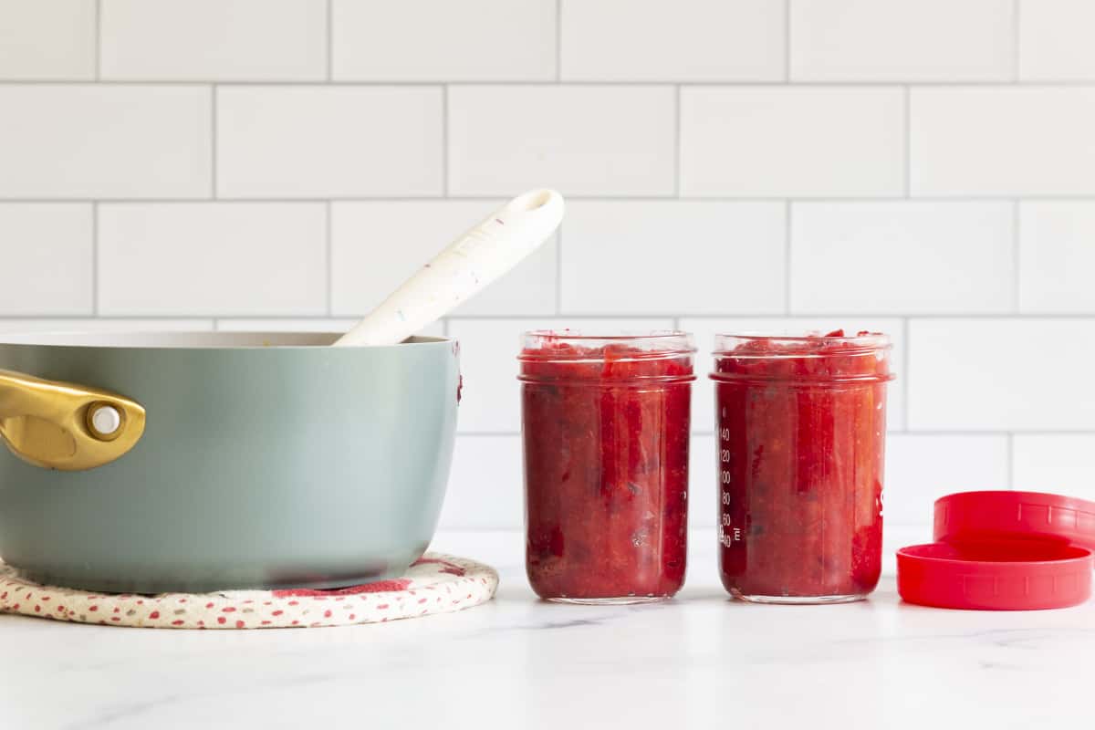 Cranberry orange sauce in two glass jars with pan.