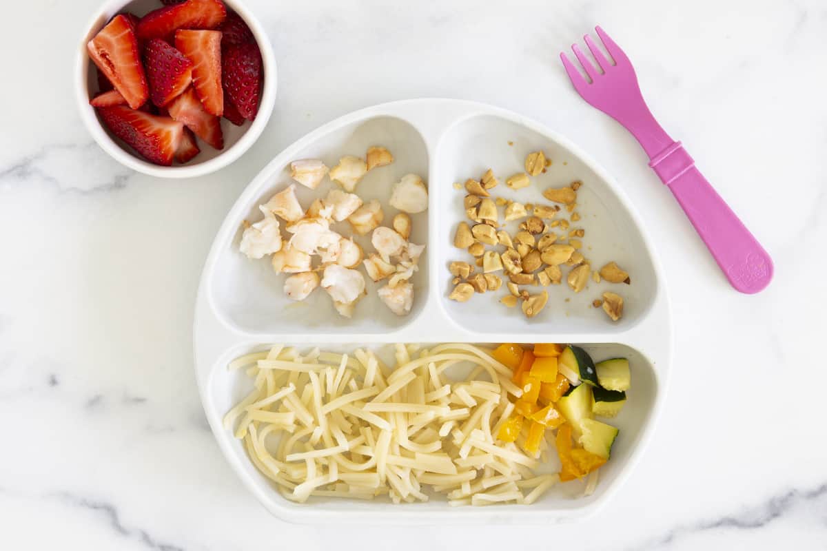 child's plate with shrimp and noodles with strawberries on side