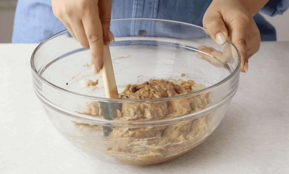 Mixing zucchini carrot muffin batter in glass bowl.