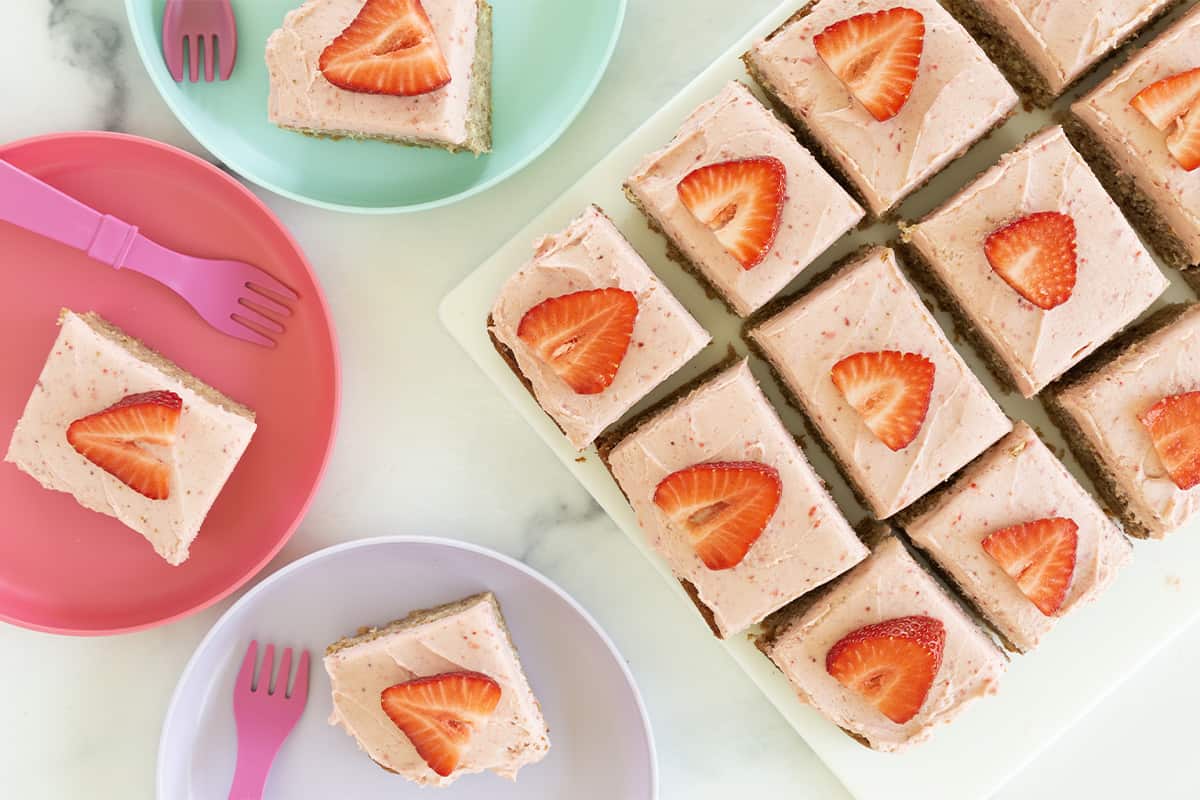 Strawberry sheet cake cut into squares on cutting board and three plates.