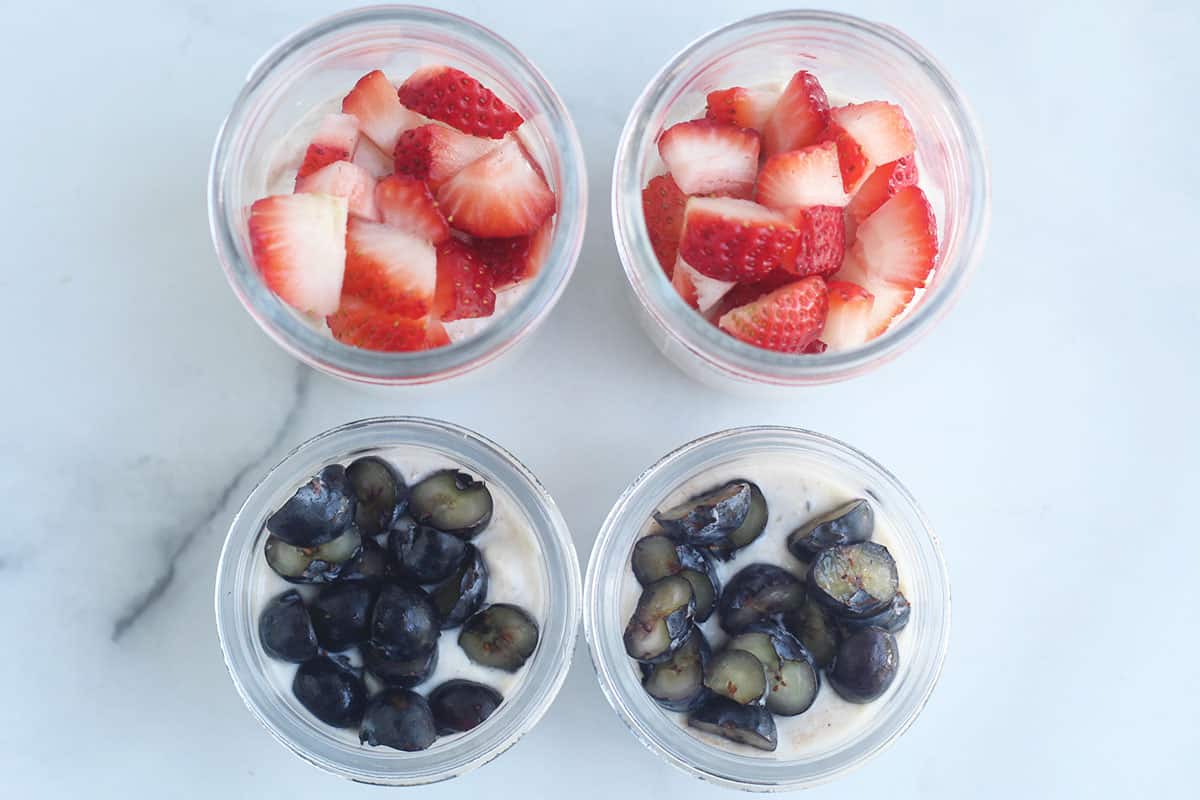overnight oats with yogurt topped with berries in four containers.