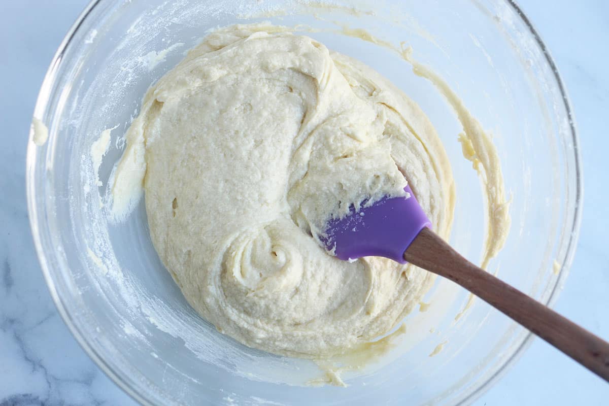 stirring batter for rainbow cake together with purple spatula.