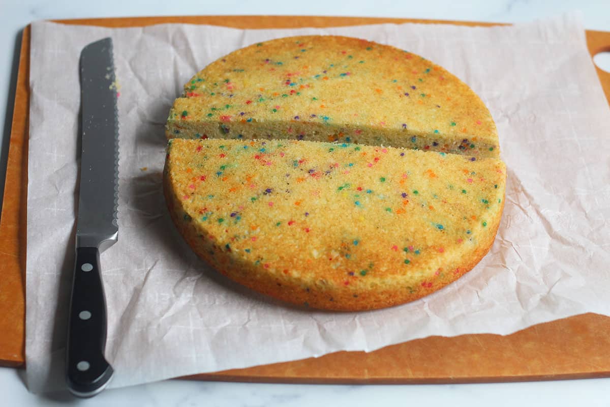 rainbow cake sliced in half on cutting board.