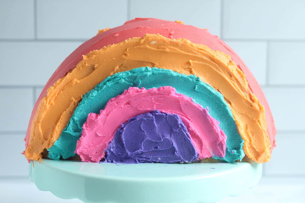 adding colors of icing to the rainbow cake on cake stand.