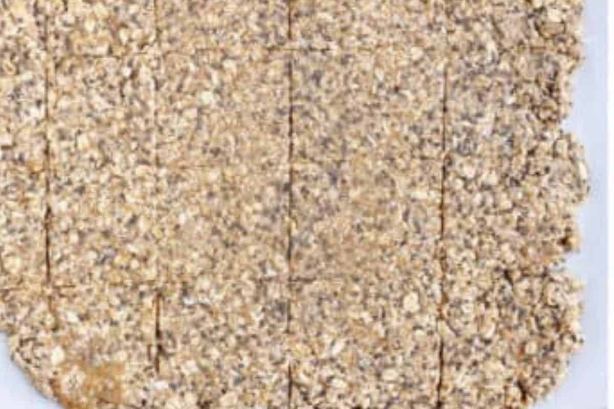 Homemade granola bars mixture spread out on parchment paper with cuts made for bars.
