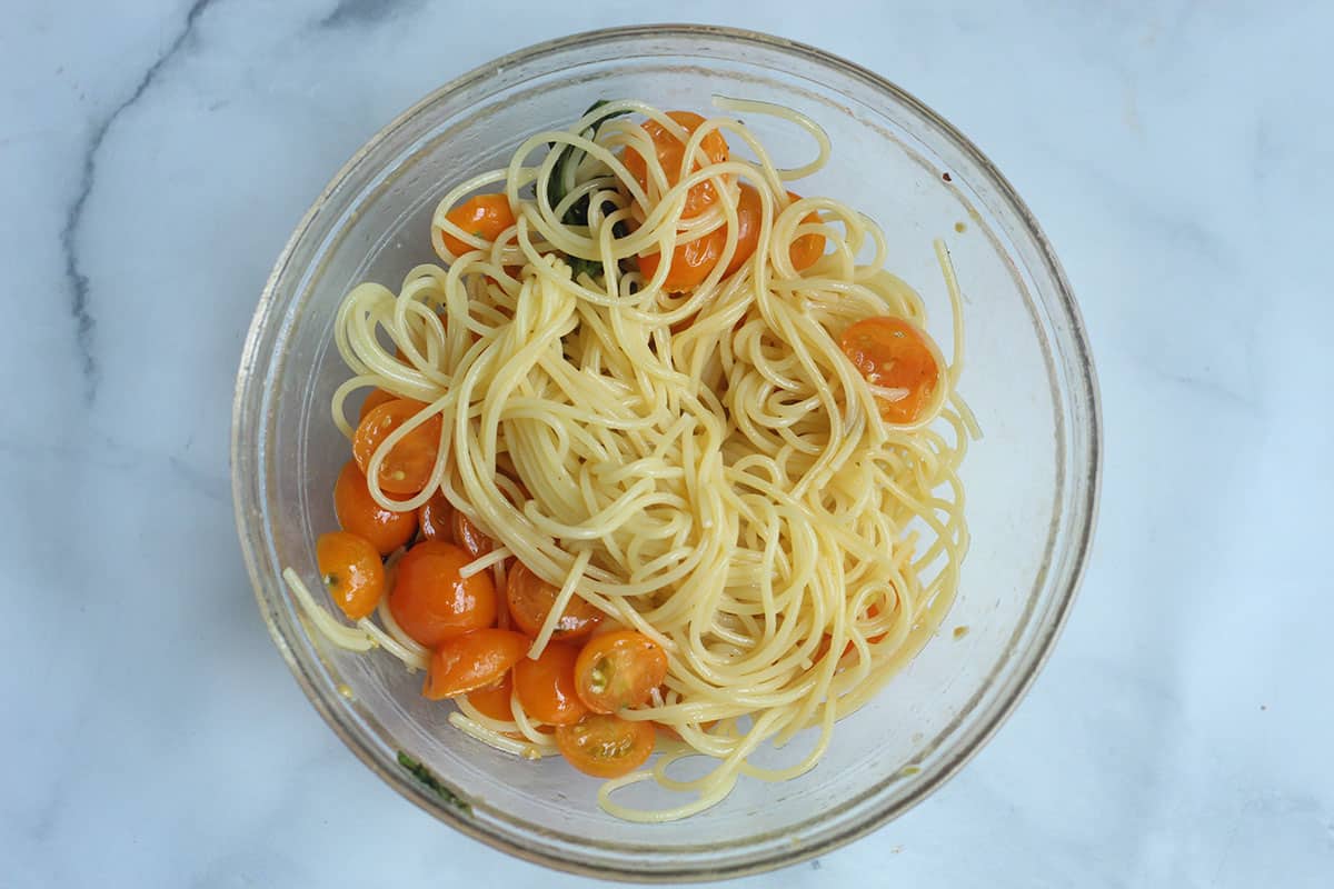 cherry tomato ingredients tossed with pasta in glass bowl.
