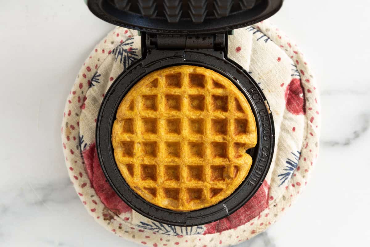 Waffle maker with sweet potato waffle in it.