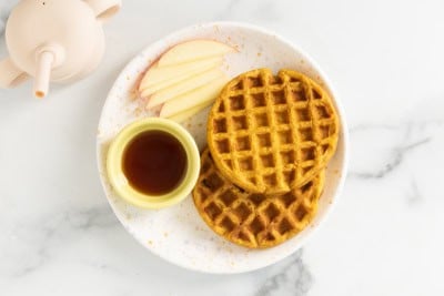 Sweet potato waffle on white plate with apple slices.