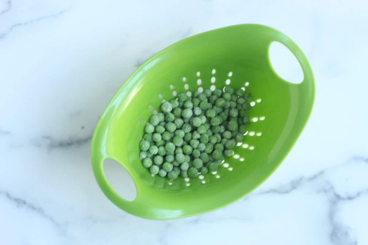 Peas in a strainer for mac and cheese with peas. 