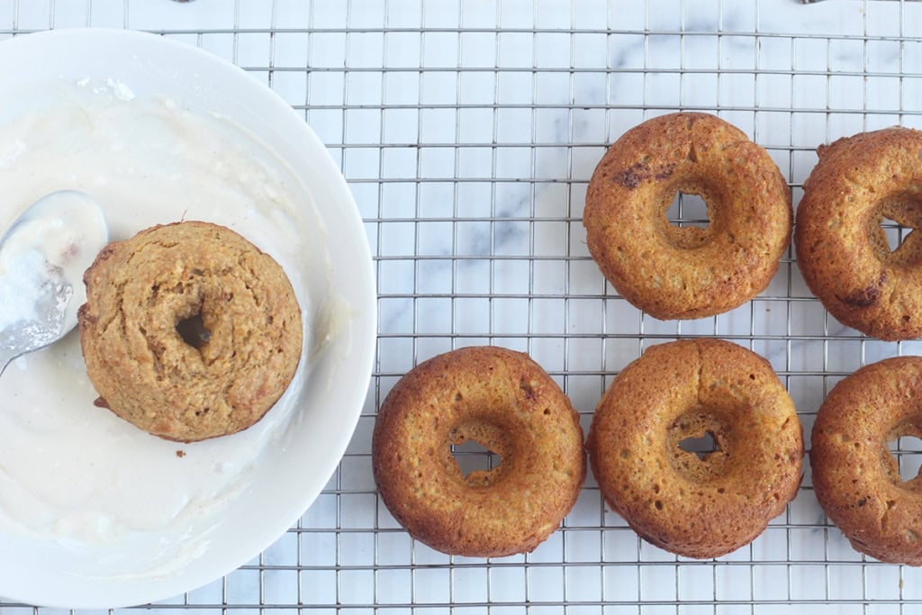 Sweet potato donuts on cooling rack being dipped in frosting.