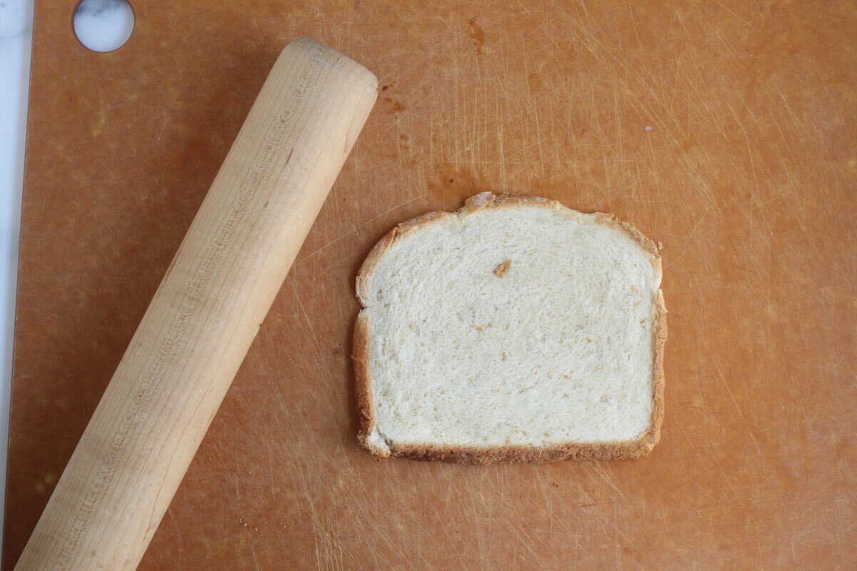 Piece of bread next to rolling pin for sandwich roll up.