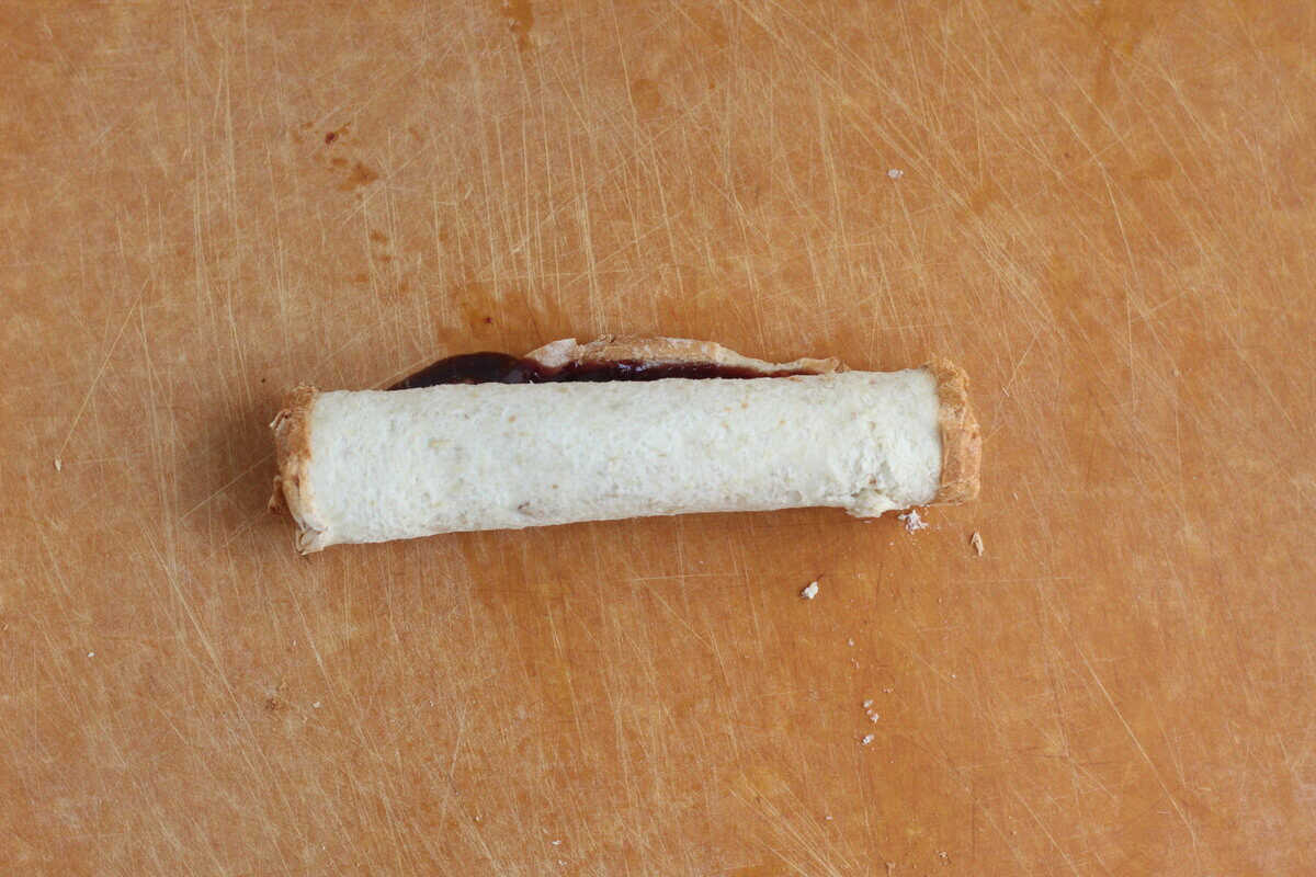 Sandwich roll up before being cut into pieces on cutting board.