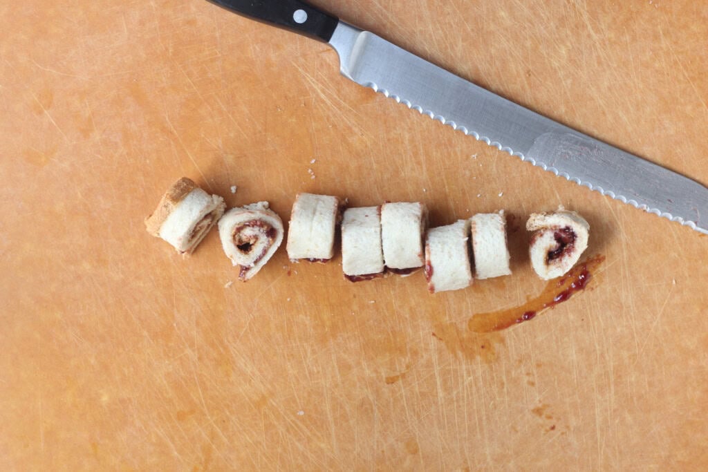 Sandwich roll-ups being cut on cutting board.