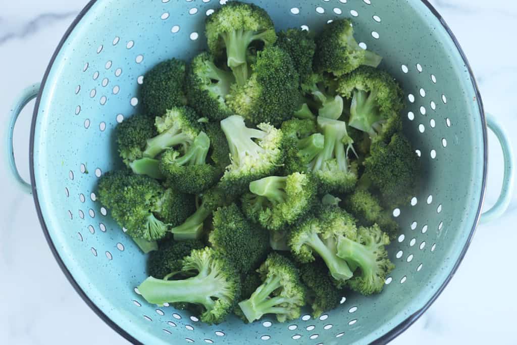 Boiled broccoli in blue colander after straining.