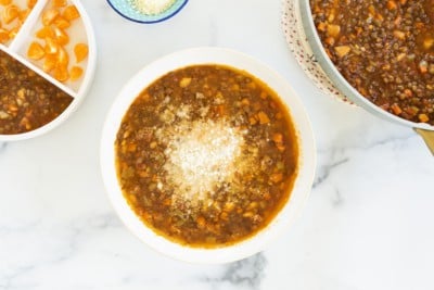 Lentil soup in white bowl with cheese on top.