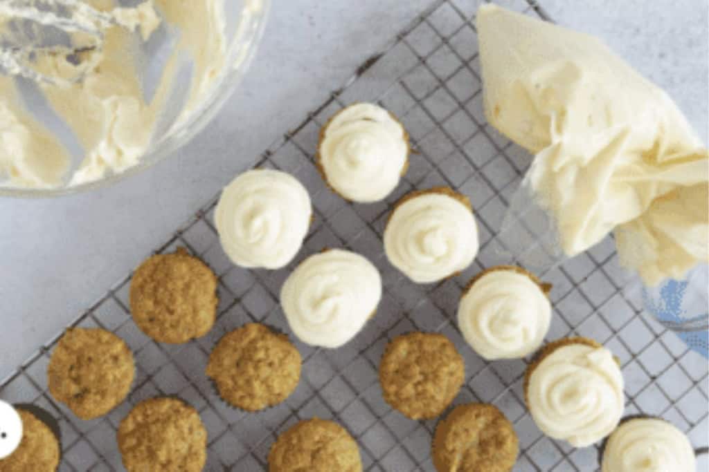 Cream cheese frosting being put onto cupcakes.