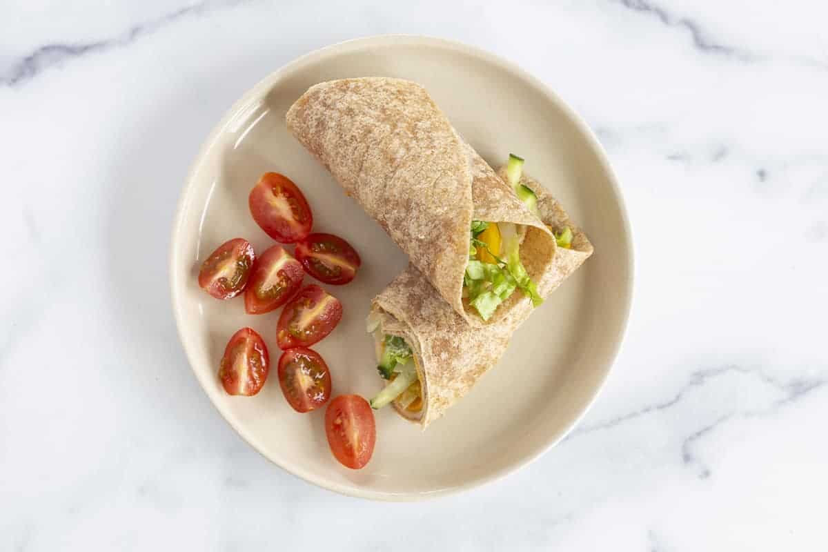 vegetarian hummus wrap on white plate with tomatoes