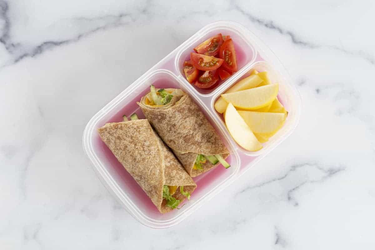 hummus wrap in lunchbox with apples and tomatoes
