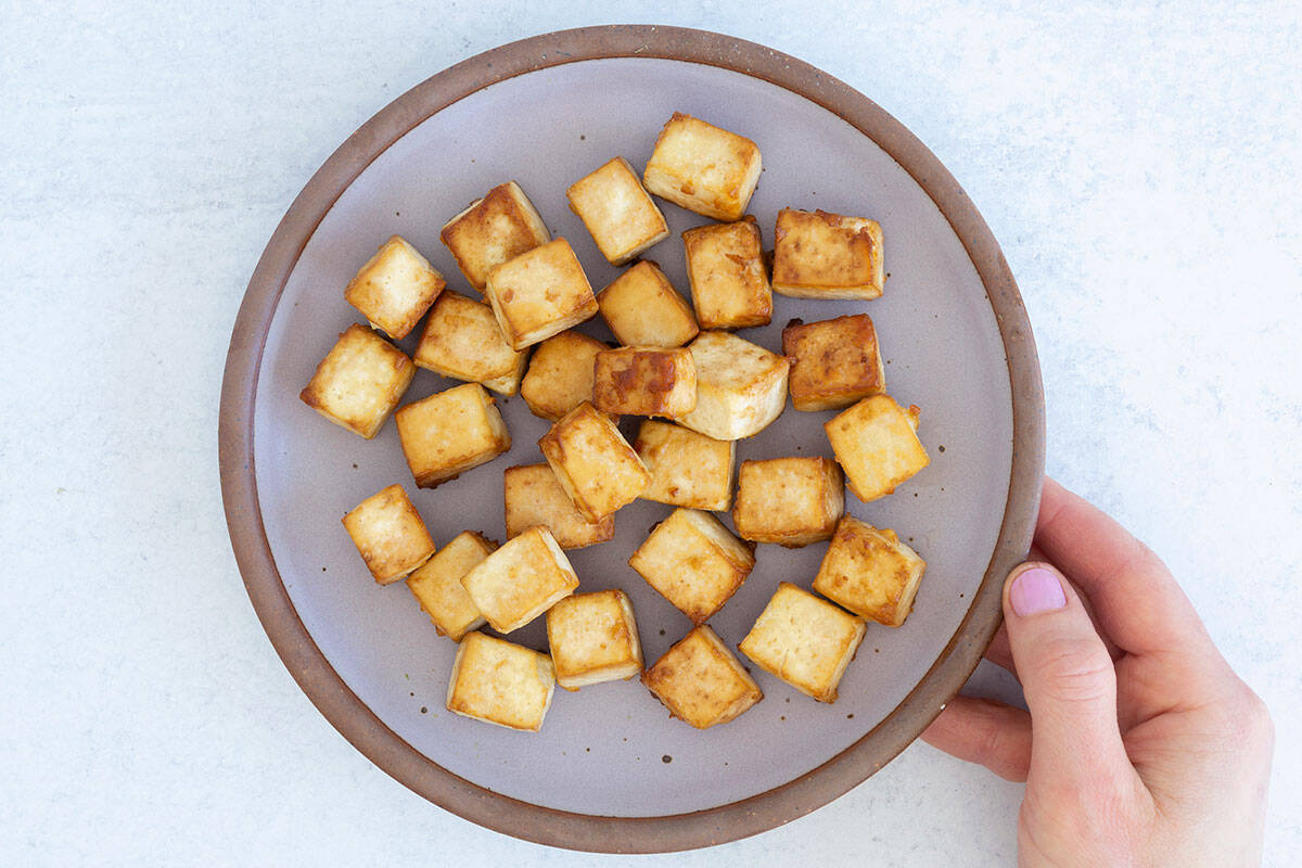 baked tofu on purple plate with hand.