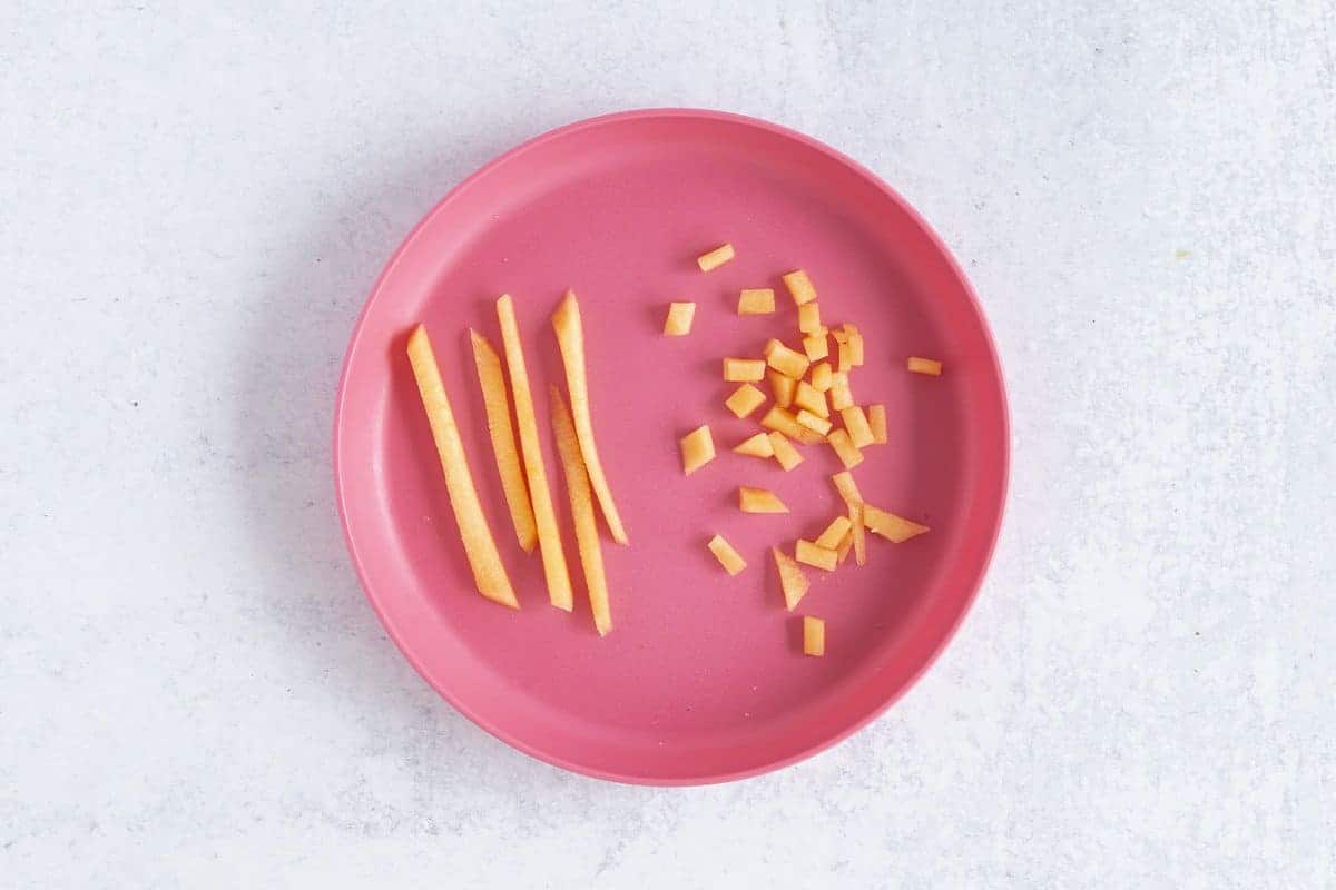 matchsticks and diced cantaloupe on pink plate.
