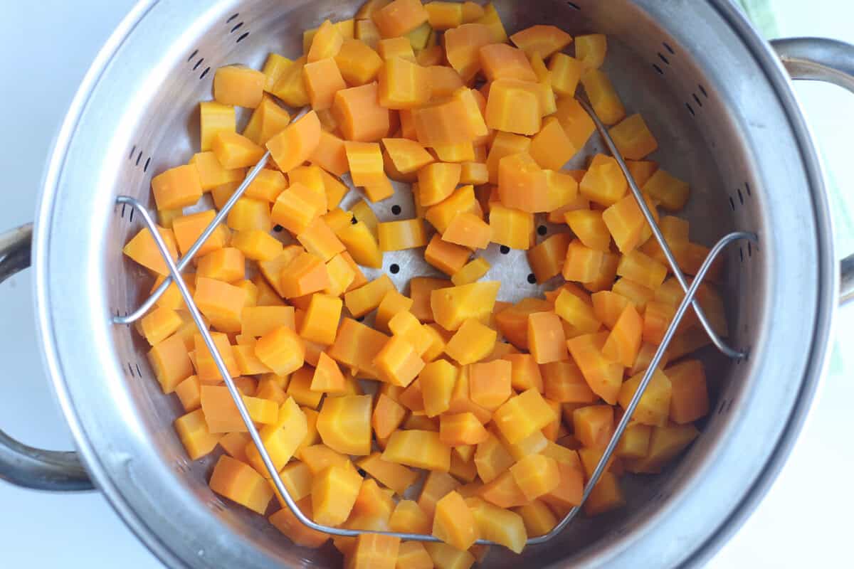 Cubbed carrots being steamed in pot for carrot puree.