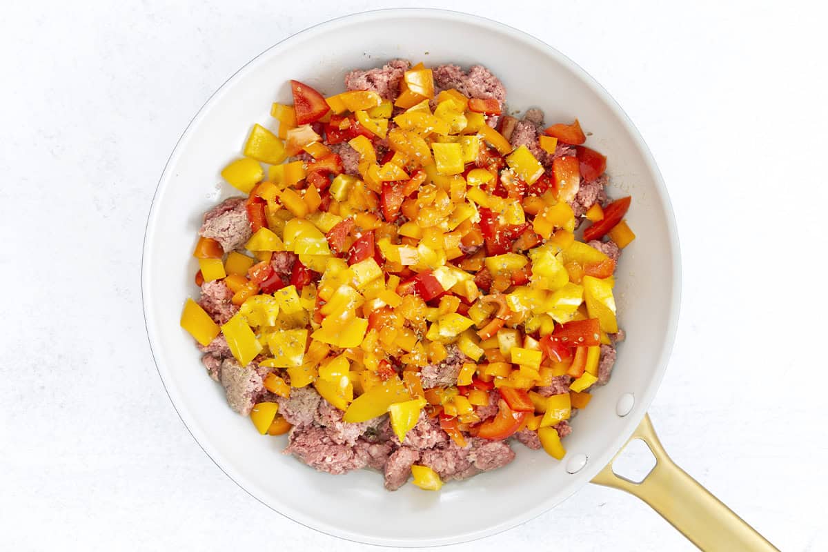 ground beef and diced peppers in white skillet.