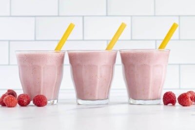 raspberry smoothies in three cups with yellow straws