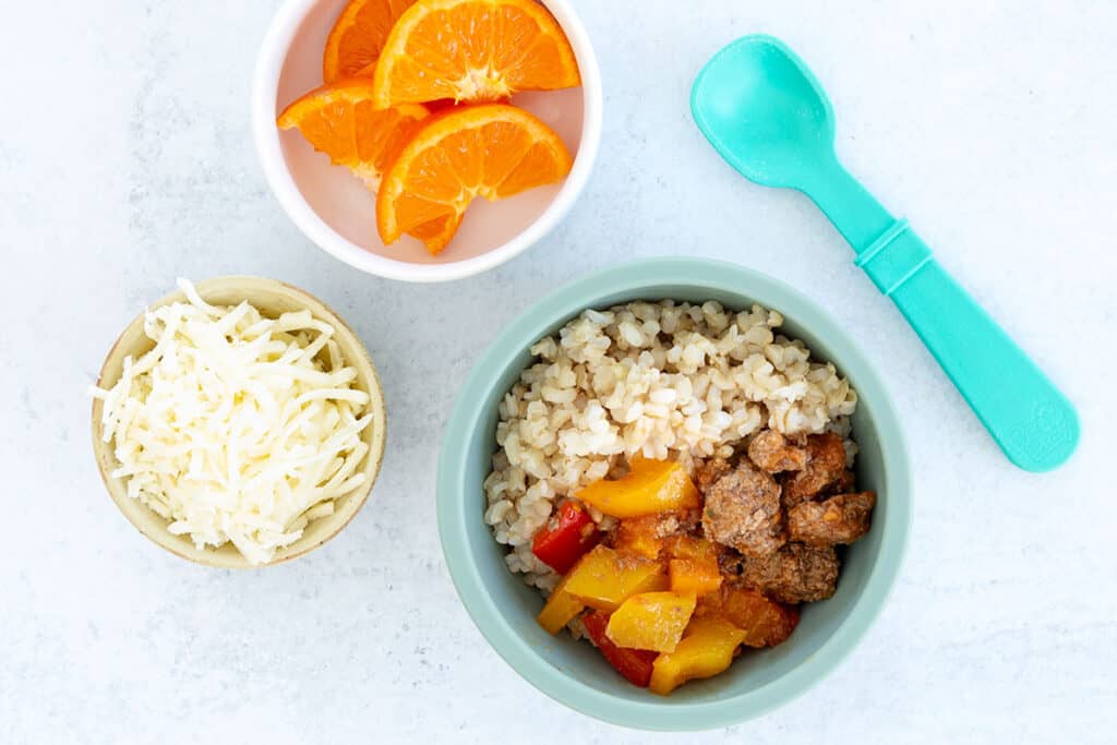 unstuffed peppers in green kids bowl with bowls of cheese and oranges.