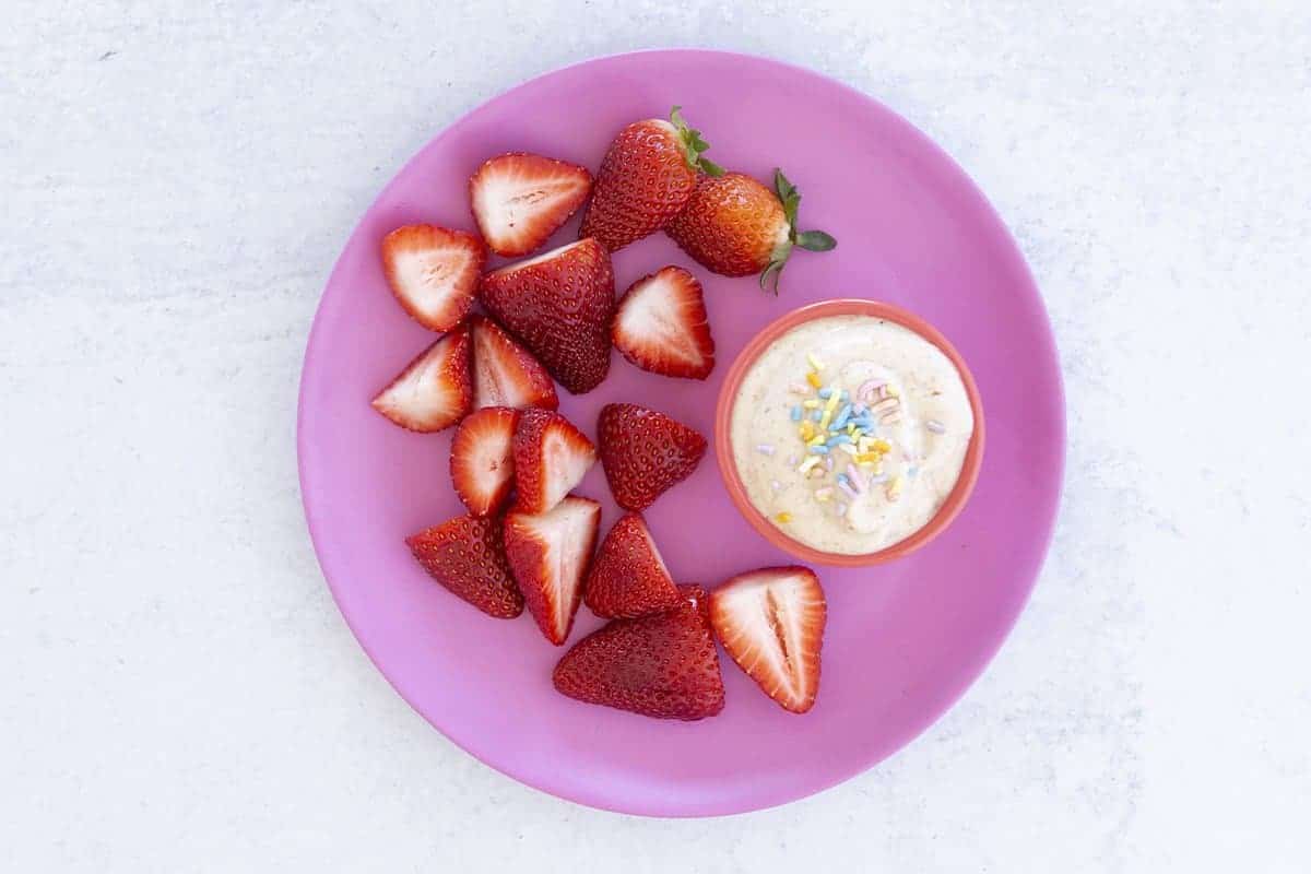 yogurt dip with strawberries on pink plate