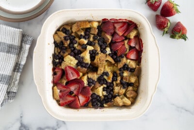 Baked french toast casserole with fruit and plates on white counter top