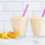 Peach smoothie in two glasses with peaches on side
