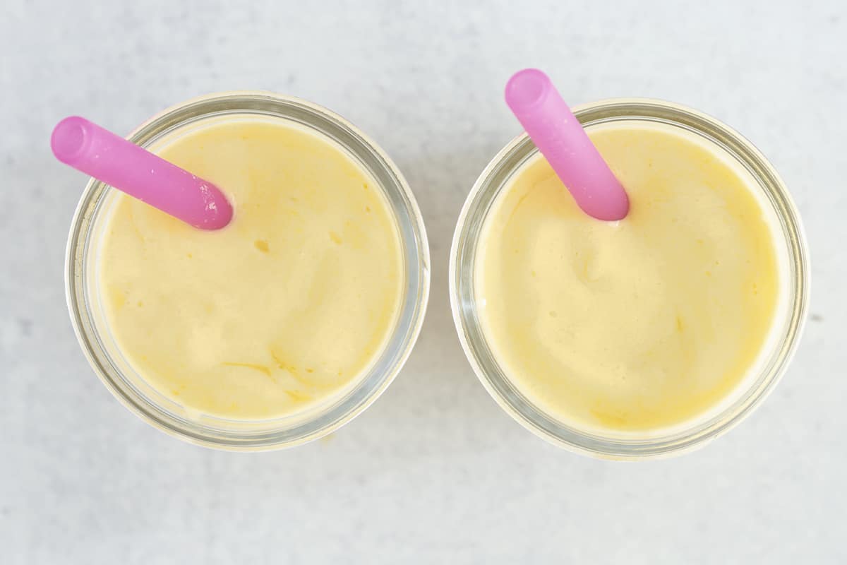 mango smoothie in two jars on counter with pink straws.