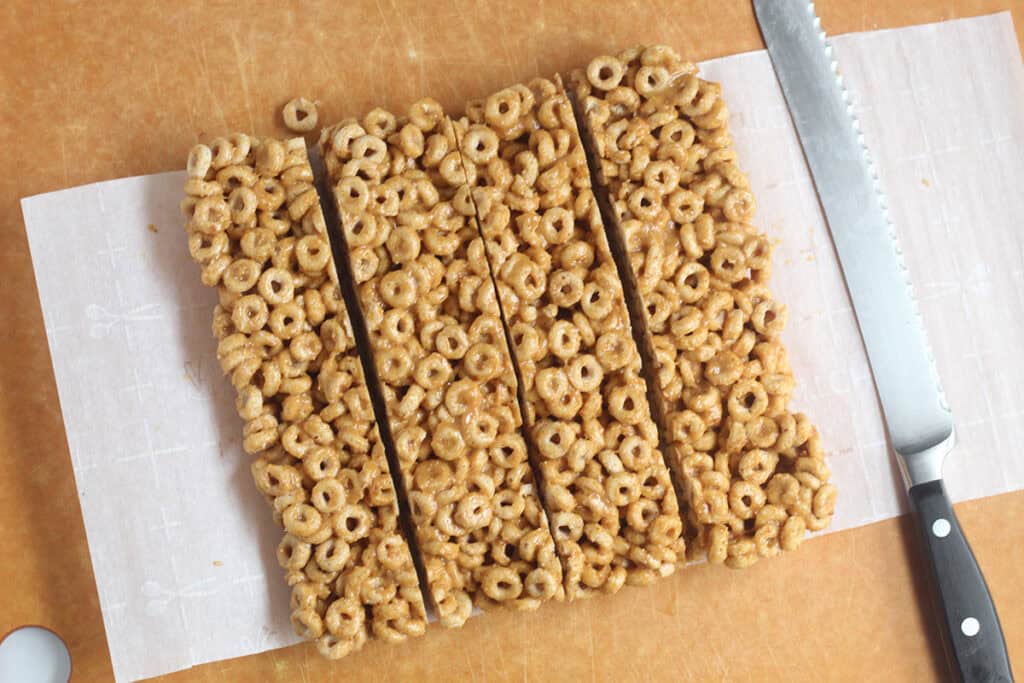 slicing cereal bars with knife on parchment paper on cutting board.