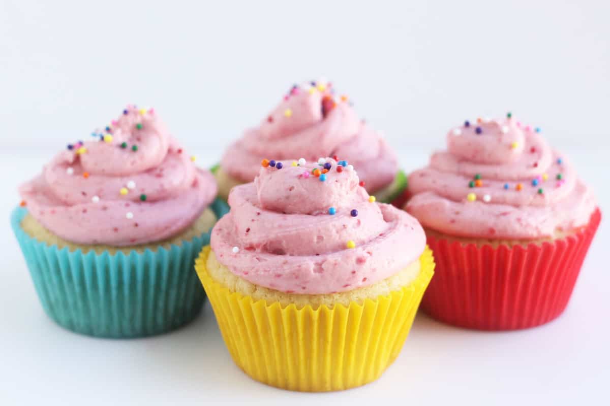 vanilla cupcakes with strawberry frosting in colored cupcake liners.