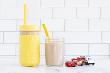 Chocolate weight gain smoothies in two glasses with straws and toy cars on the side