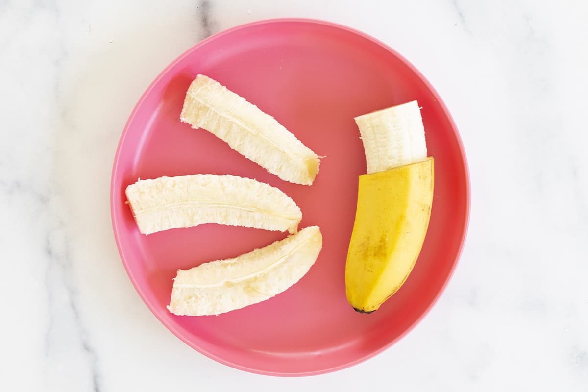 Banana half with peel and banana slices on red plate for blw banana