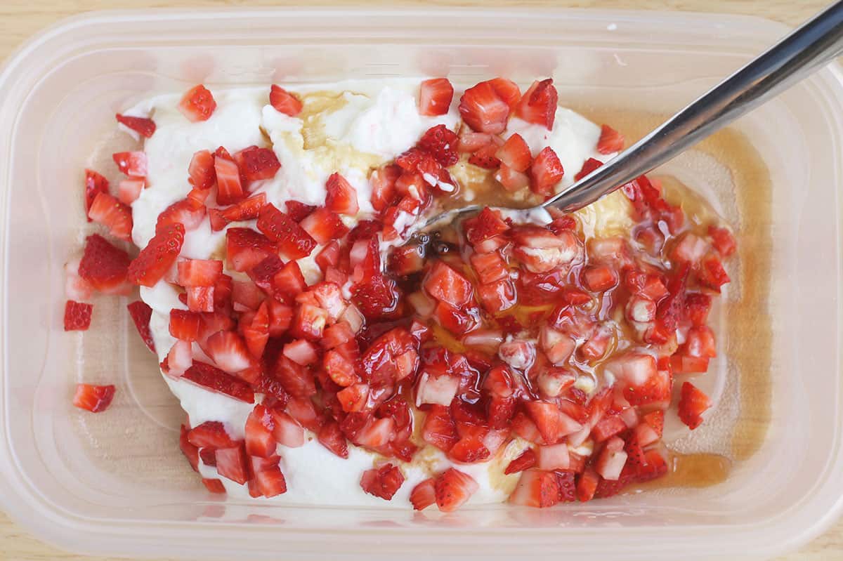 stirring ingredients for strawberry frozen yogurt in freezer container