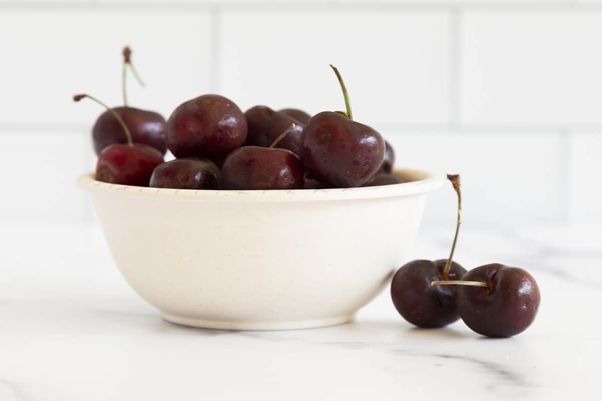 Whole cherries in white bowl with stems
