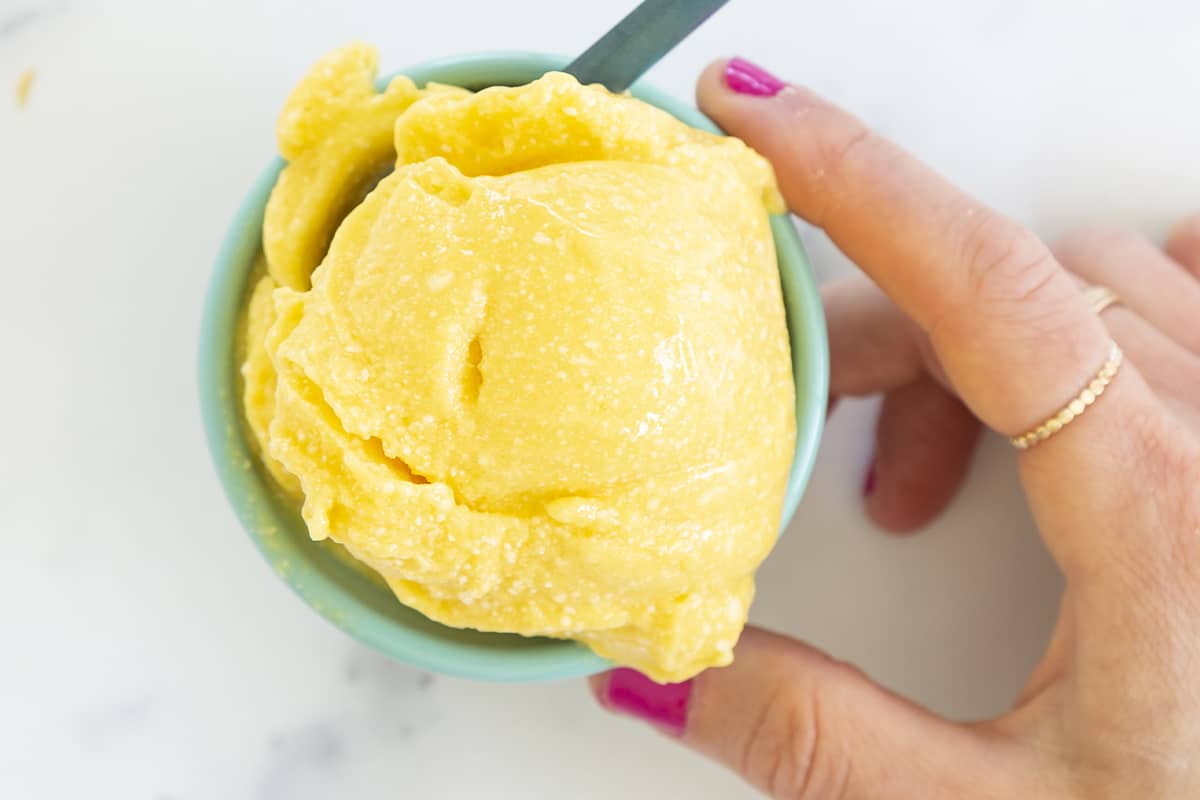 mango sorbet in blue bowl with hand holding bowl from above